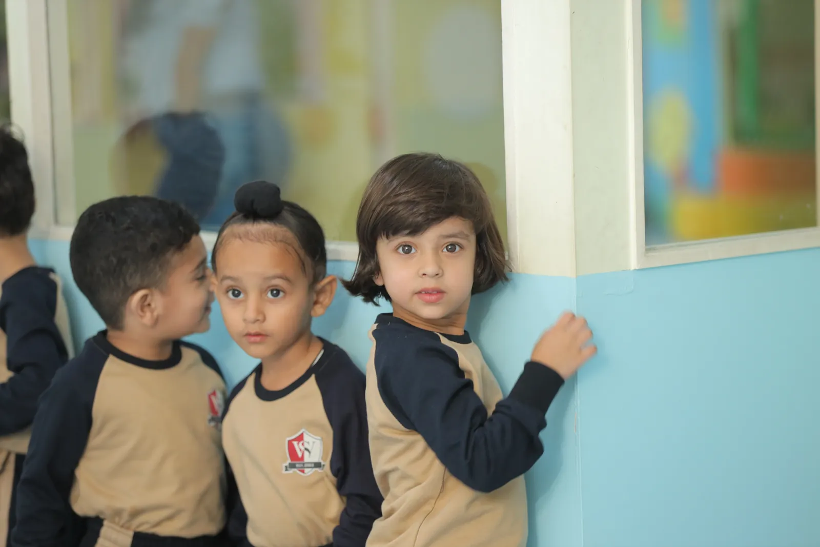 Three young learners in Small Wonders uniform at a classroom wall.