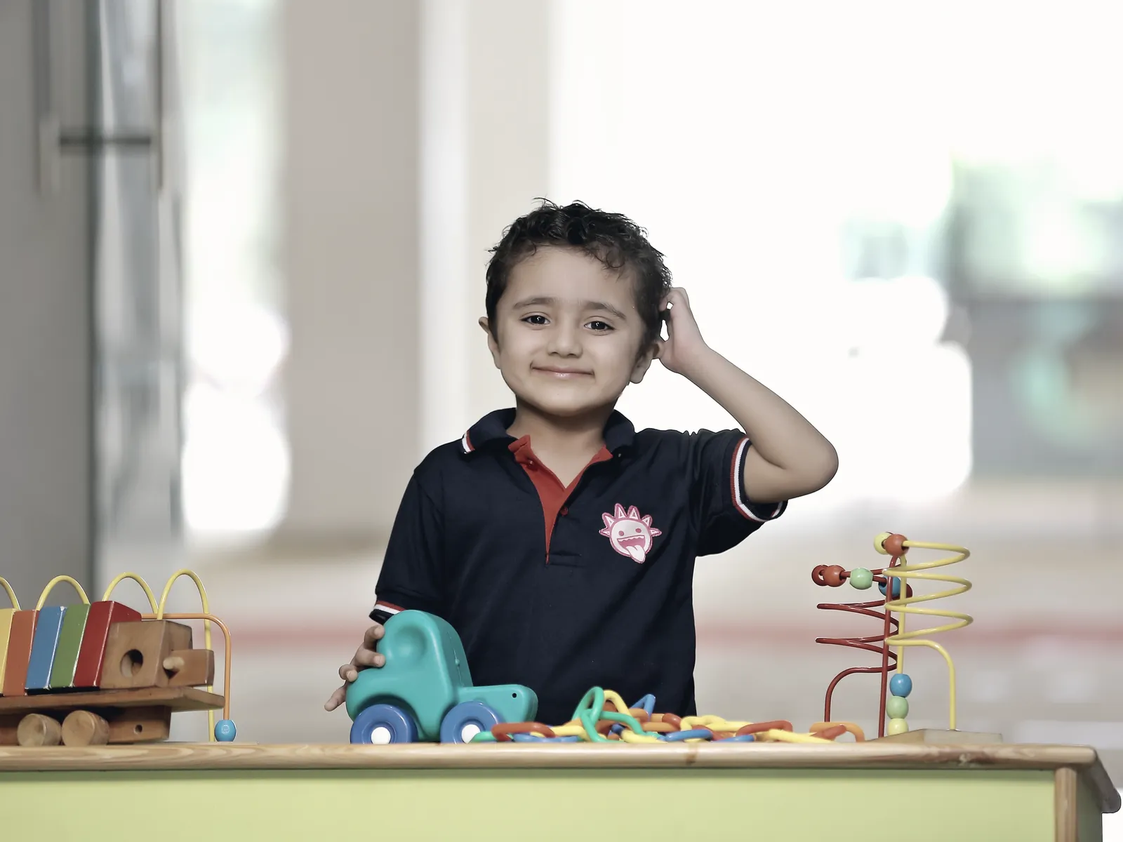A learner at a low table, choosing between a xylophone, a wooden truck and a bead frame.